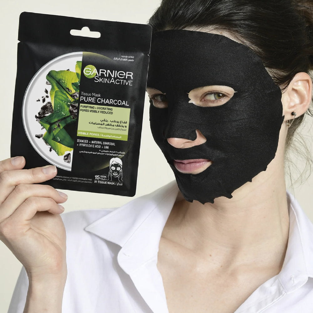 Person wearing a black face mask with Garnier SkinActive Pure Charcoal packaging.